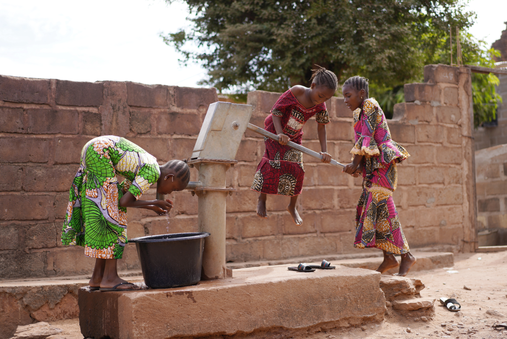 girls utilize a water pump to fill a bucket.
