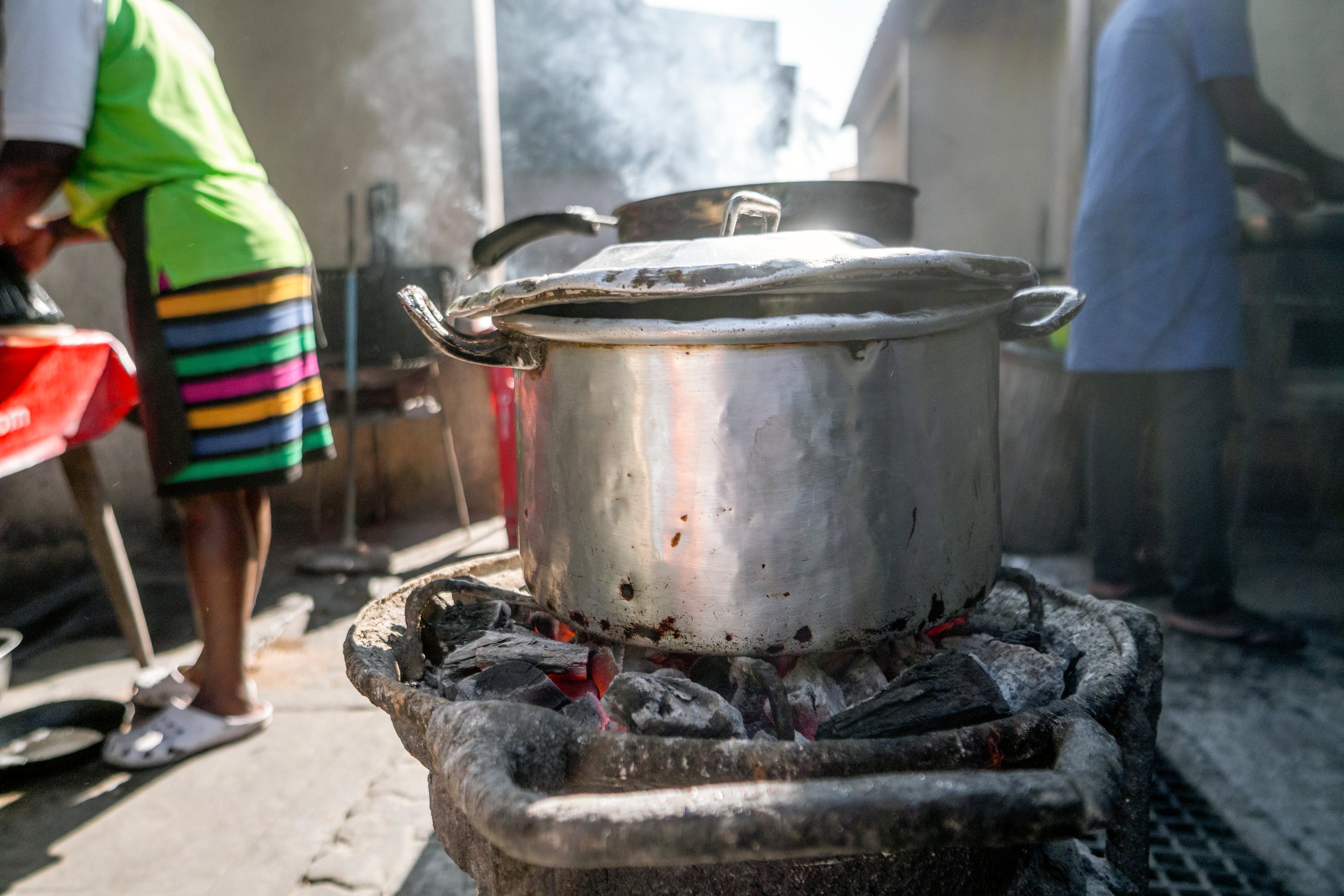 a silver pot simmers over coals in a traditional cookstove in a kitchen.