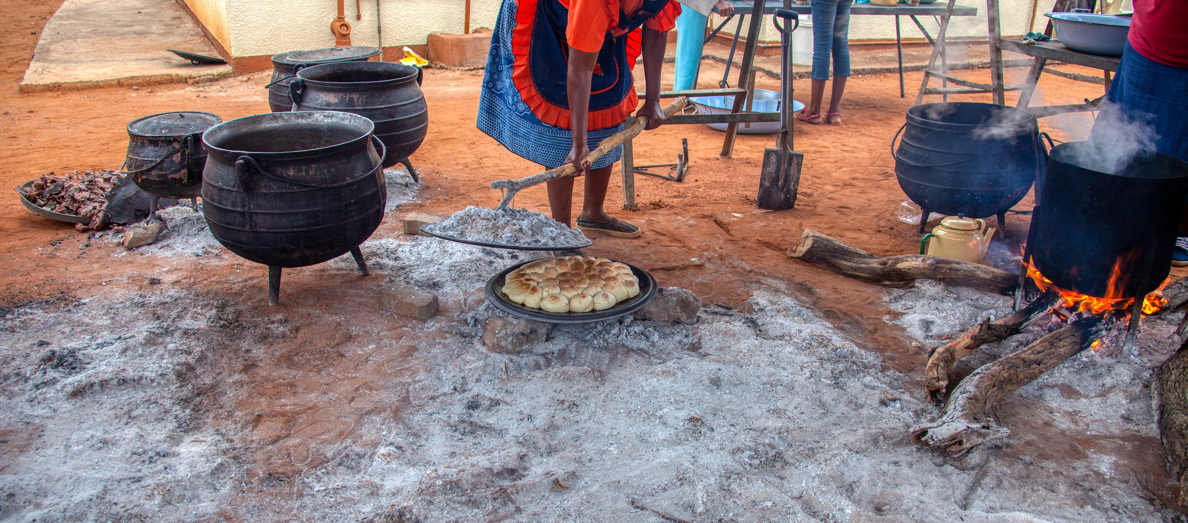 people cooking outdoors in large black pots upon open flames.