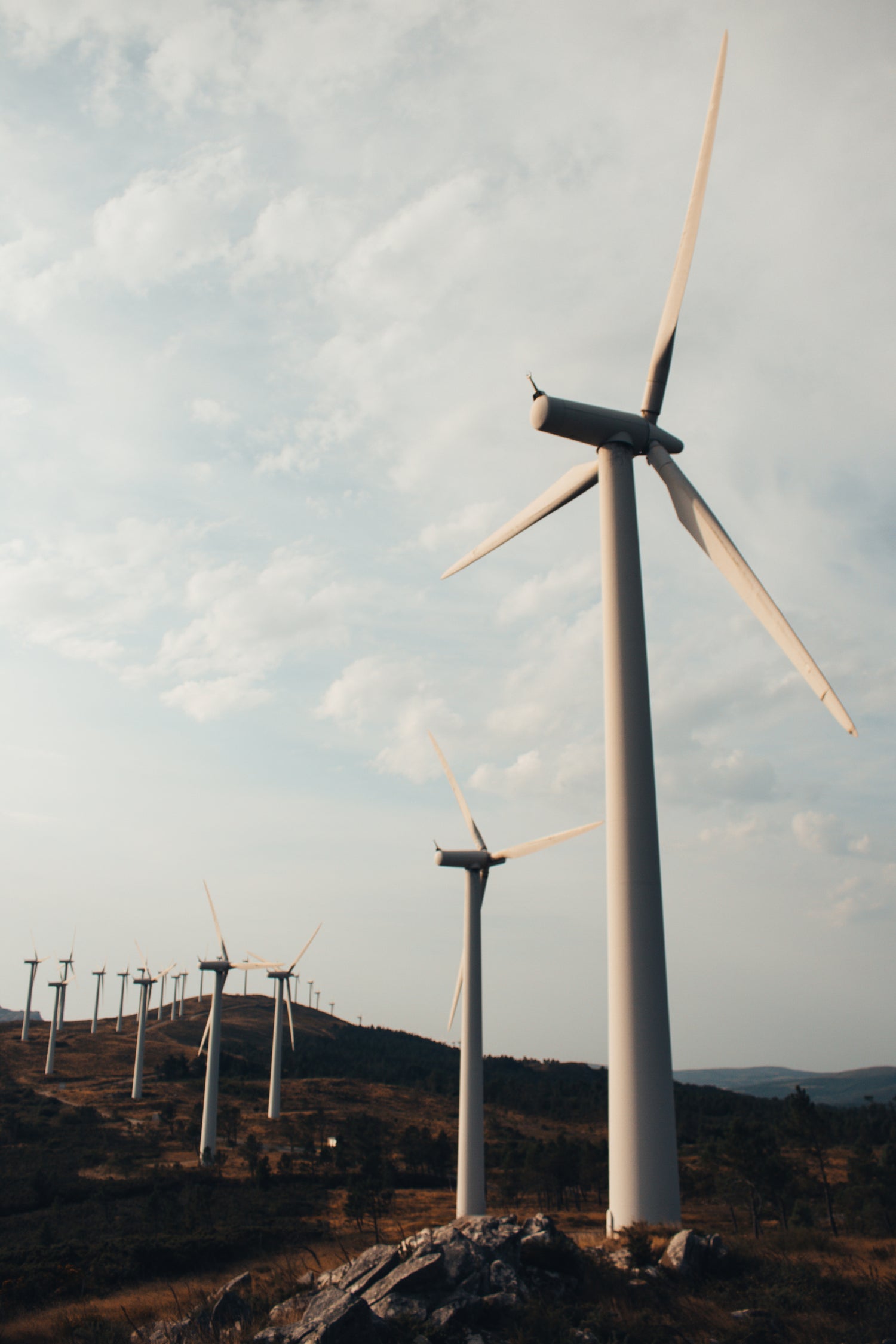 wind turbines on a mountain ridge in the sunlight with the sky above them.