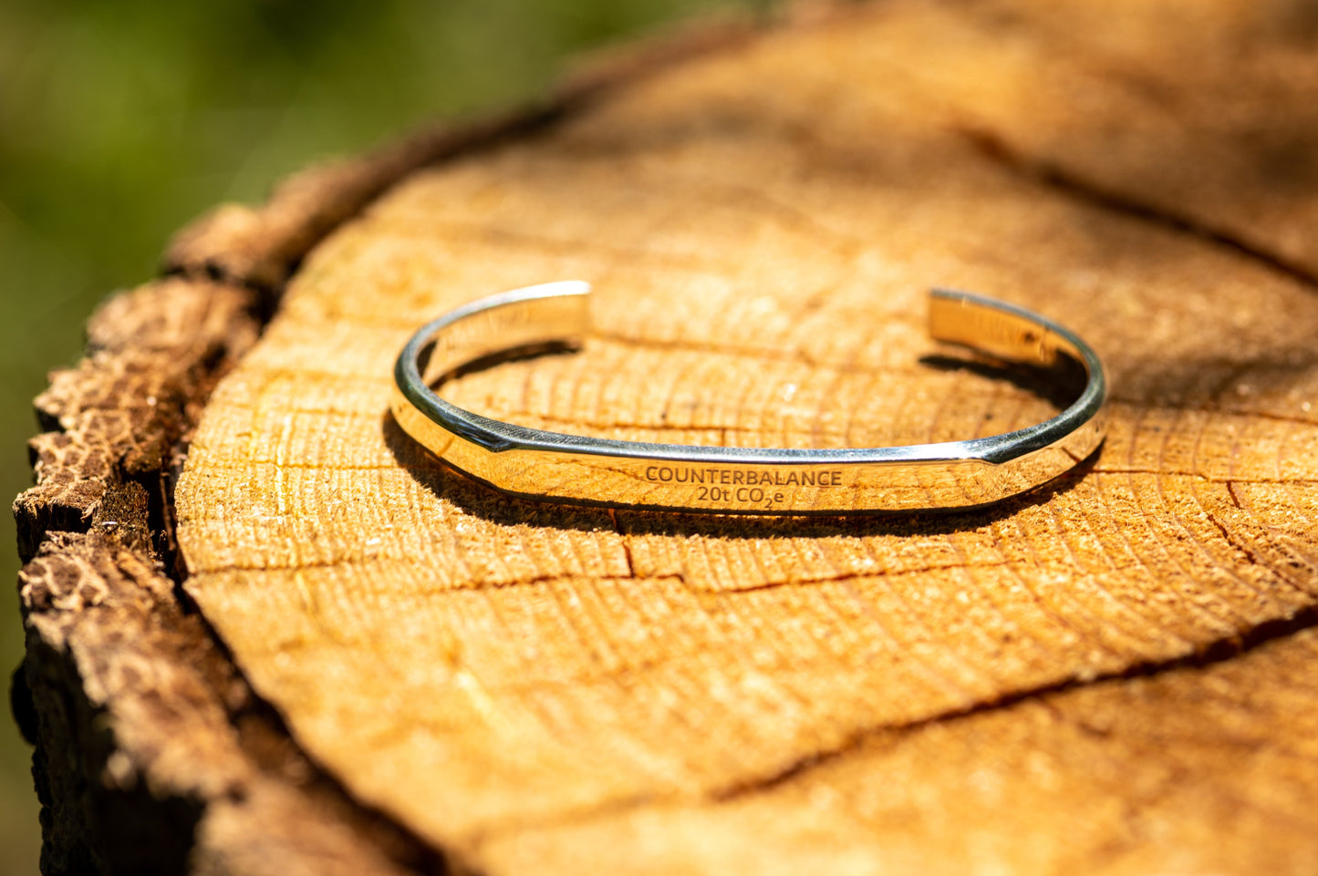 A silver counterbalance bracelet engraved with the word Counterbalance and the abbreviation 20t CO2e for 20 tons of carbon dioxide equivalent. The bracelet is displayed on a pine tree's exposed rings.