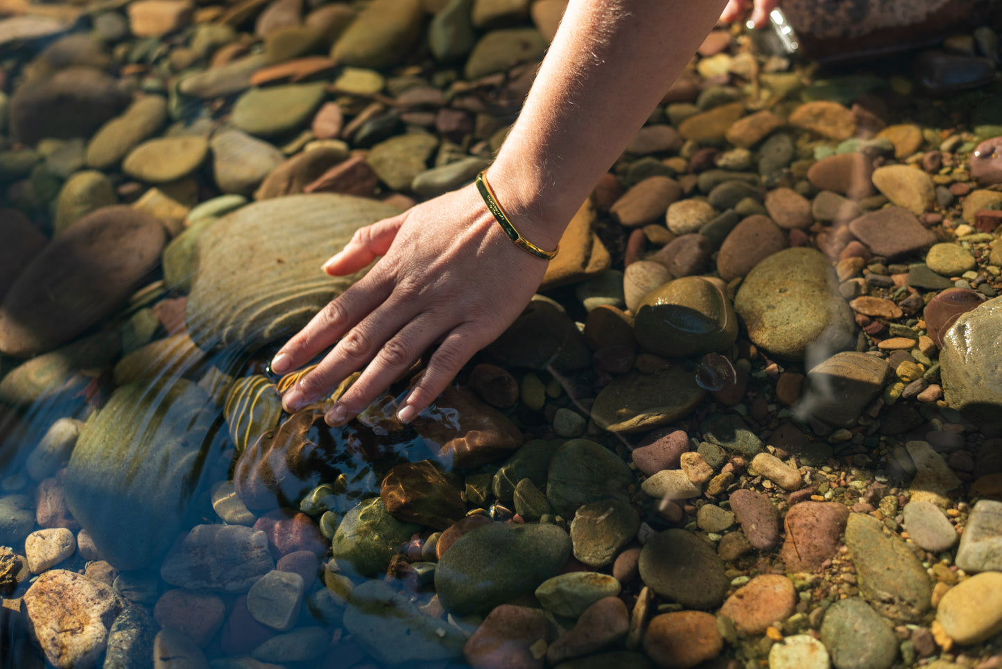 A model wearing the yellow gold counterbalance bracelet creates ripples in the still water of a rocky creek bed.