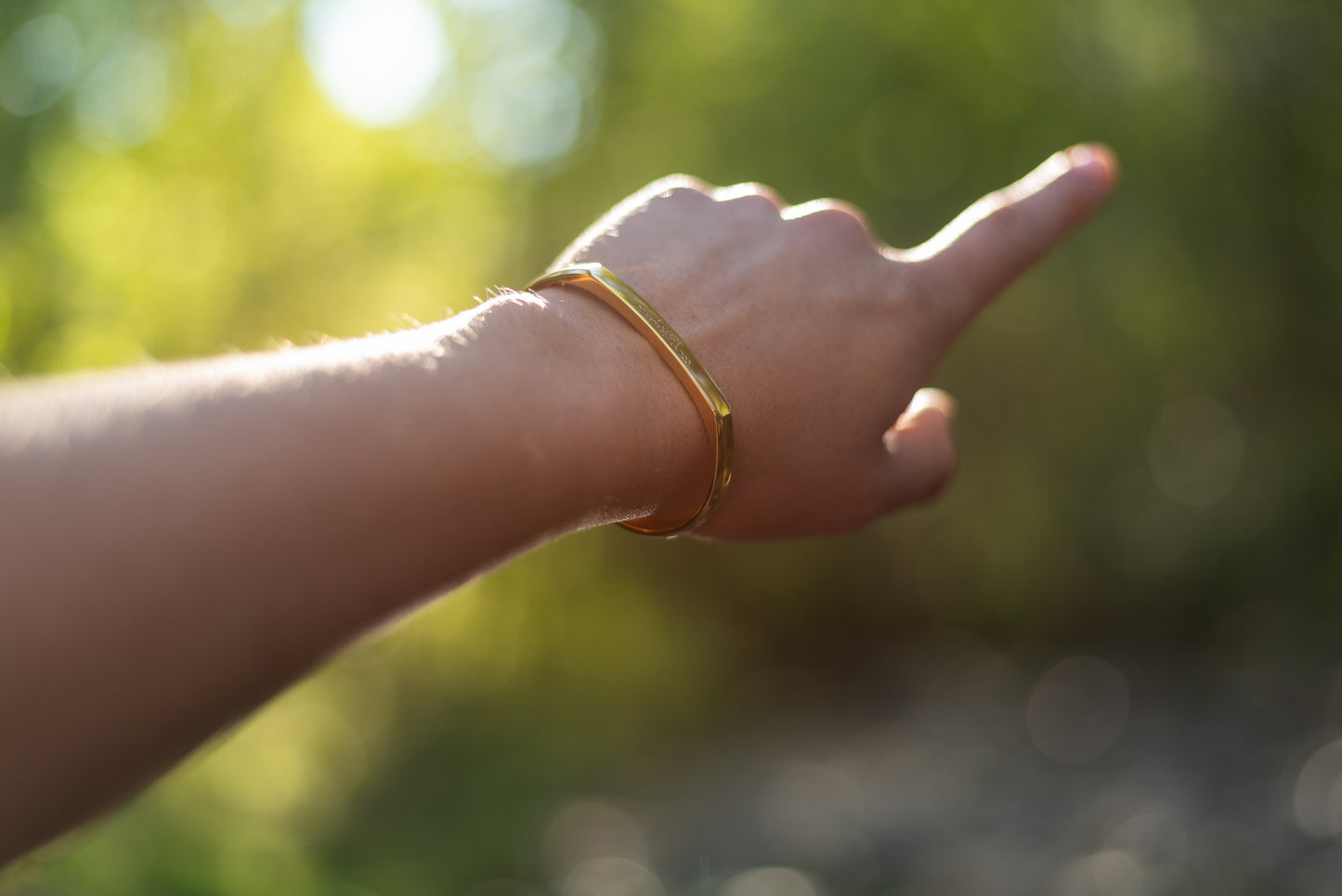 A model wearing the yellow gold counterbalance bracelet gestures towards the forest.