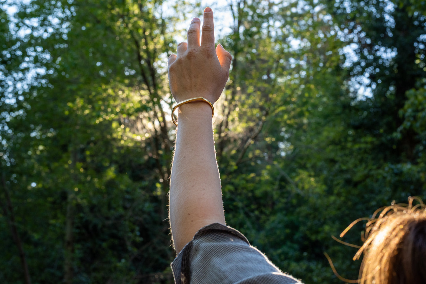 A model wearing the yellow gold counterbalance bracelet gestures towards the forest.