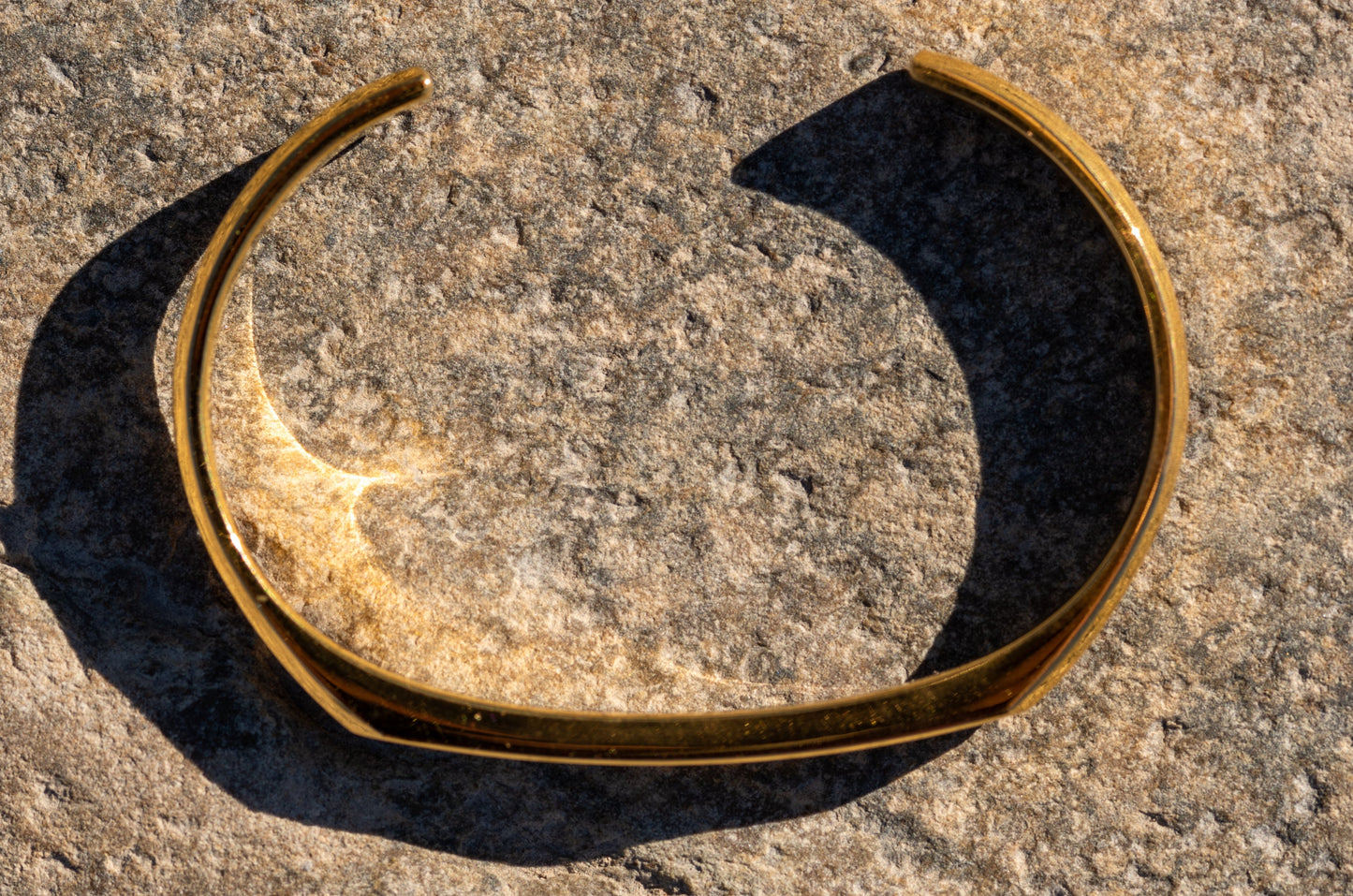 A gold counterbalance bracelet is viewed from an aerial top-down view on a natural rock surface.
