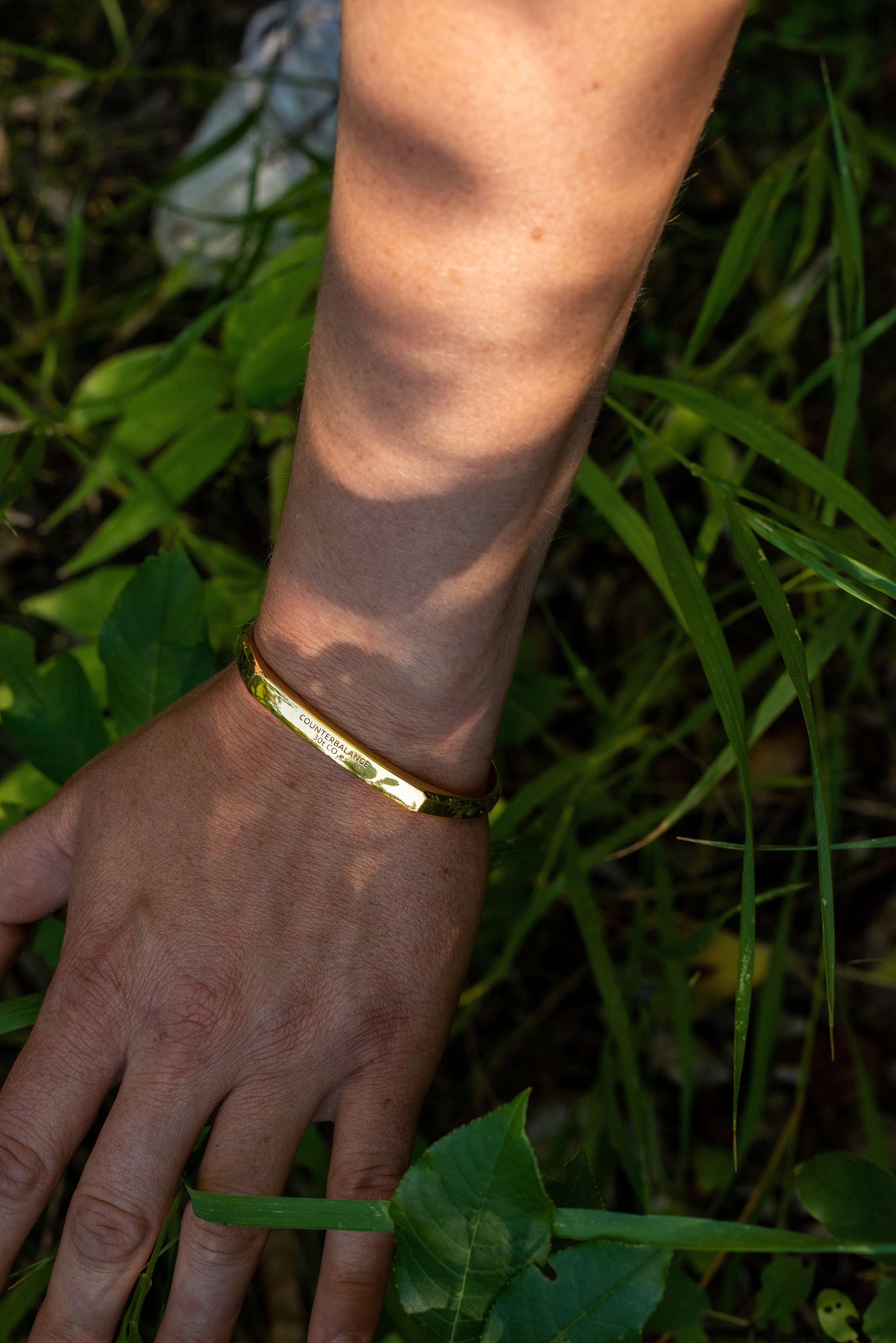 A modle wearing the yellow gold counterbalance bracelet reaches towards green blades of grass