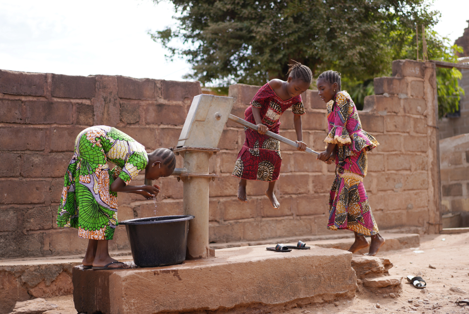 girls utilize a water pump to fill a bucket. 