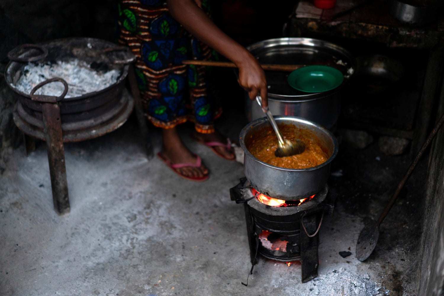 a woman stirs a pot of foods that simmers above a flame on an improved/ efficient cookstove. 