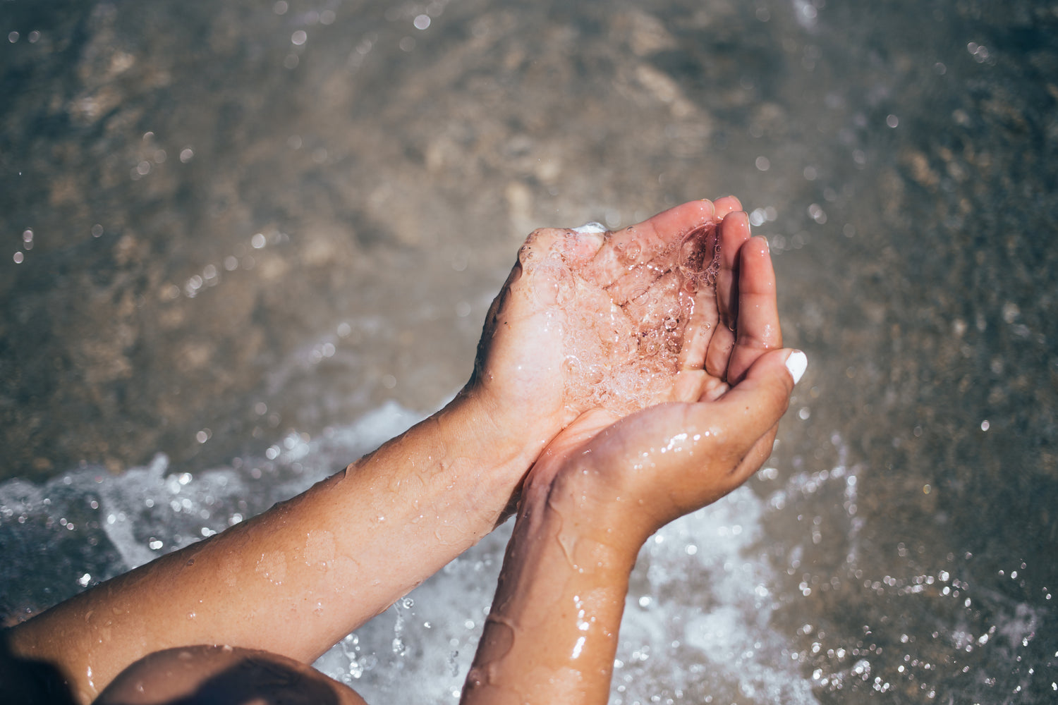 water droplets flow through the fingers of a woman's hands. 