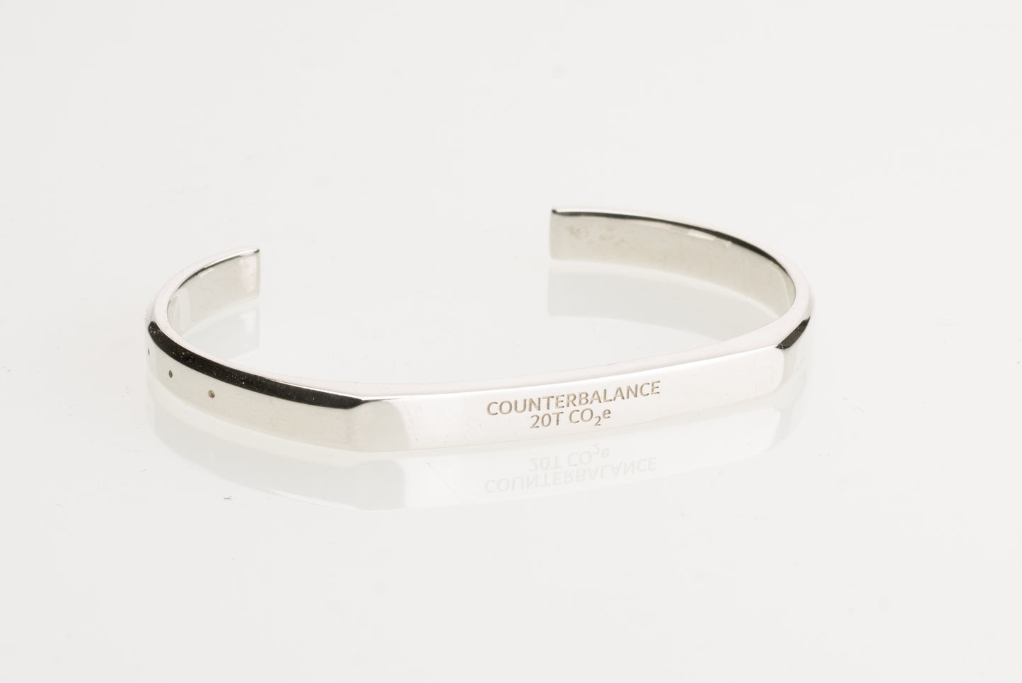 A silver counterbalance bracelet engraved with the word Counterbalance and the abbreviation 20t CO2e for 20 tons of carbon dioxide equivalent. The bracelet is displayed on a reflective white surface.