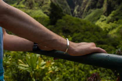 A silver counterbalance bracelet engraved with the word Counterbalance and the abbreviation 20t CO2e for 20 tons of carbon dioxide equivalent. The bracelet is displayed on a model's wrist with green foliage in the background.