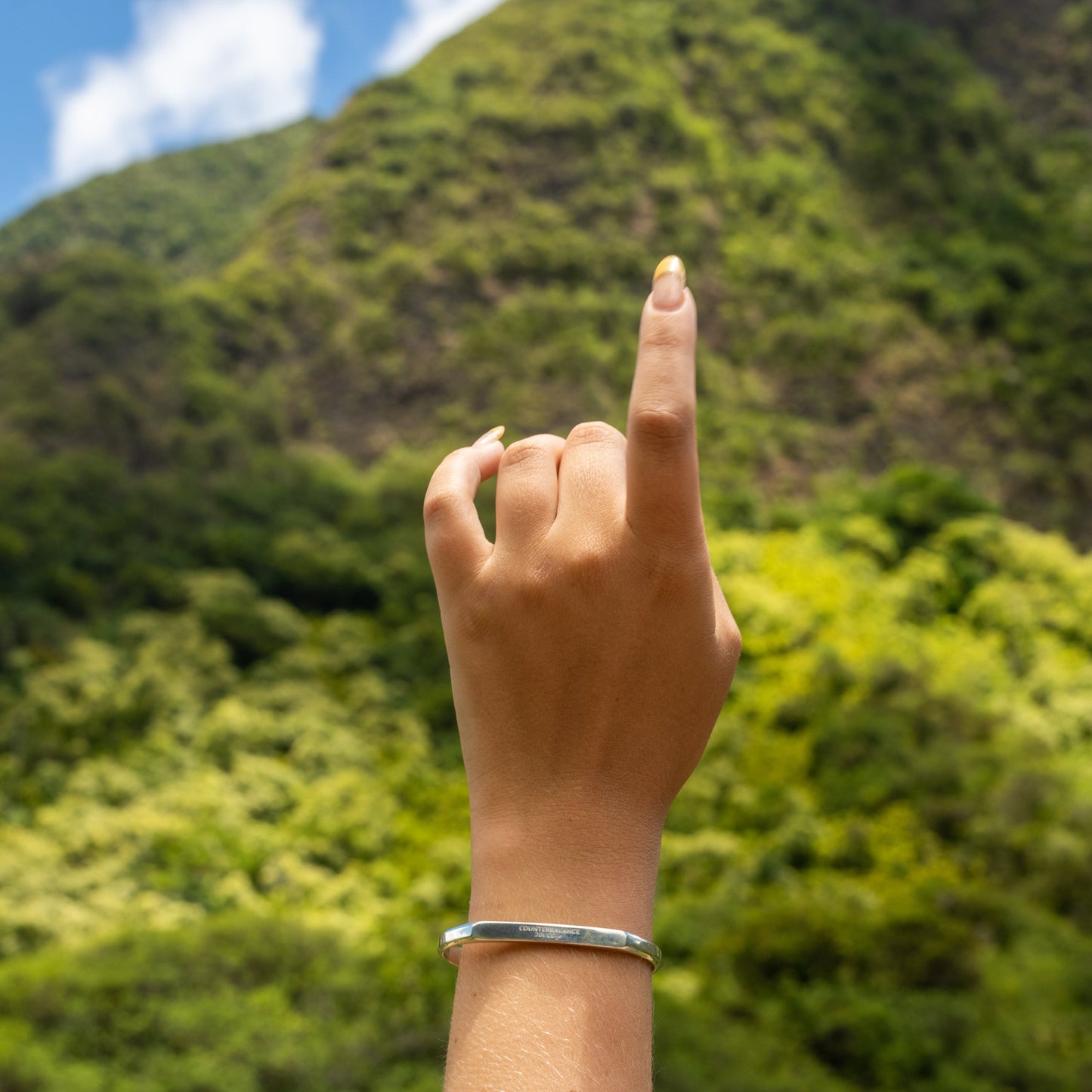 A silver counterbalance bracelet engraved with the word Counterbalance and the abbreviation 20t CO2e for 20 tons of carbon dioxide equivalent. The bracelet is displayed on a model's wrist with green foliage in the background.