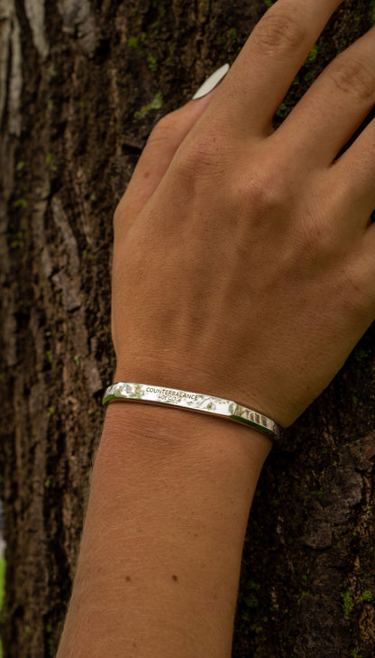 A model wears the white gold counterbalance while resting their hand upon a tree trunk.