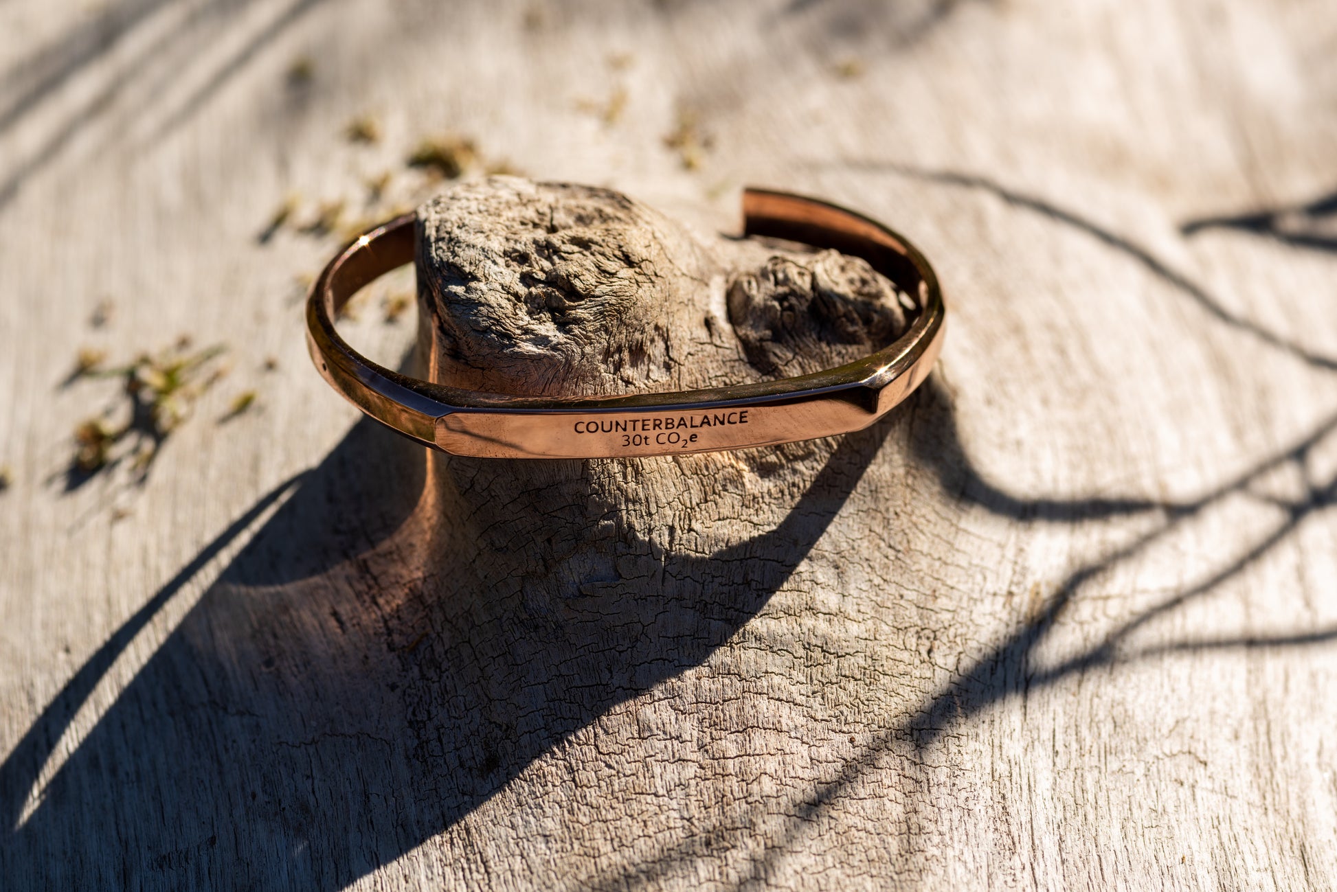 A rose gold counterbalance bracelet displayed upon piece of driftwood on the riverbank of the clark fork river. The bracelet is engraved with the word Counterbalance with the abbreviations and symbols for 30 tons of carbon dioxide equivalent below it.