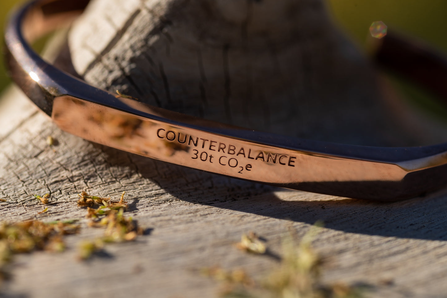 A rose gold counterbalance bracelet displayed upon piece of driftwood on the riverbank of the clark fork river. The bracelet is engraved with the word Counterbalance with the abbreviations and symbols for 30 tons of carbon dioxide equivalent below it.