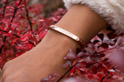 A rose gold counterbalance bracelet engraved with the word Counterbalance with the abbreviations and symbols for 30 tons of carbon dioxide equivalent below it. The bracelet is worn by a model, seen on their wrist with red foliage in the background.