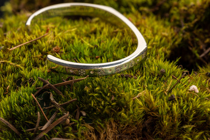 A 20 ton silver counterbalance bracelet displayed on a bed of moss.