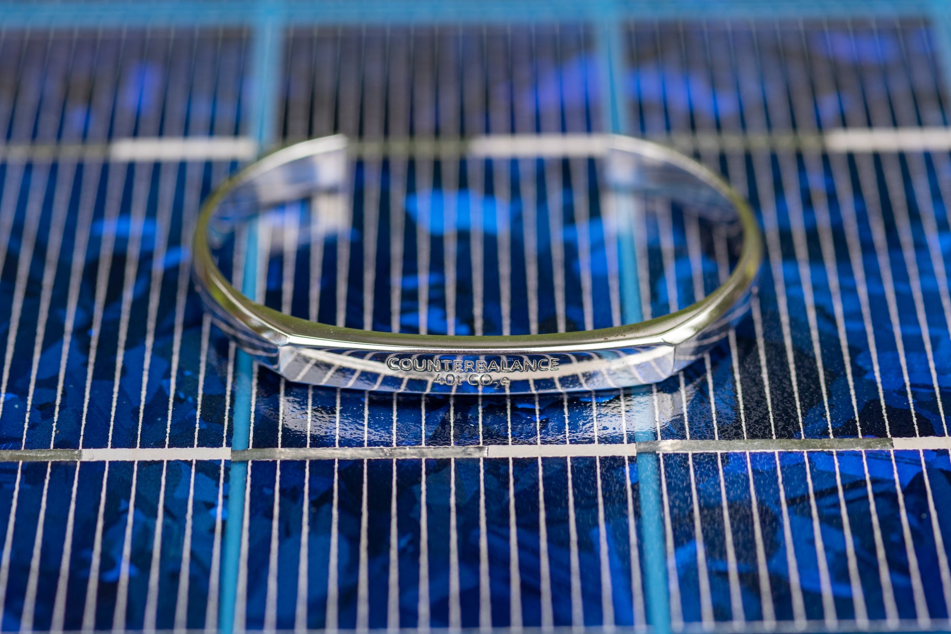 A white gold counterbalance bracelet engraved with 40t CO2e for 40 tons of carbon dioxide equivalent. The bracelet is displayed upon a blue solar panel. 