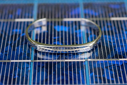 A white gold counterbalance bracelet engraved with 40t CO2e for 40 tons of carbon dioxide equivalent. The bracelet is displayed upon a blue solar panel. 