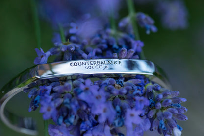 A white gold counterbalance bracelet engraved with 40t CO2e for 40 tons of carbon dioxide equivalent. The bracelet rests upon the flowers of a lavender plant.