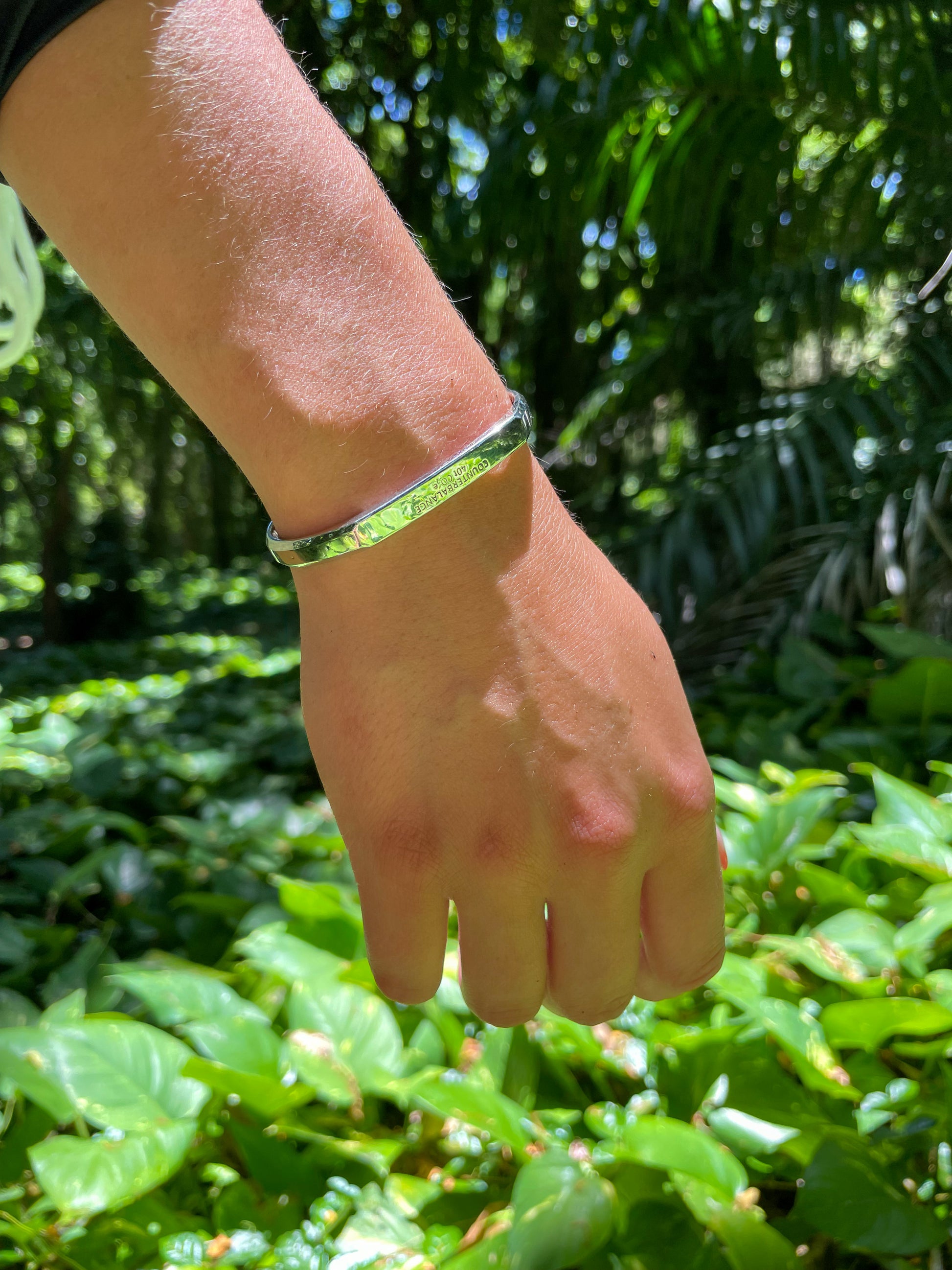 A model wears the white gold counterbalance with a lush rainforest floor in the background. 